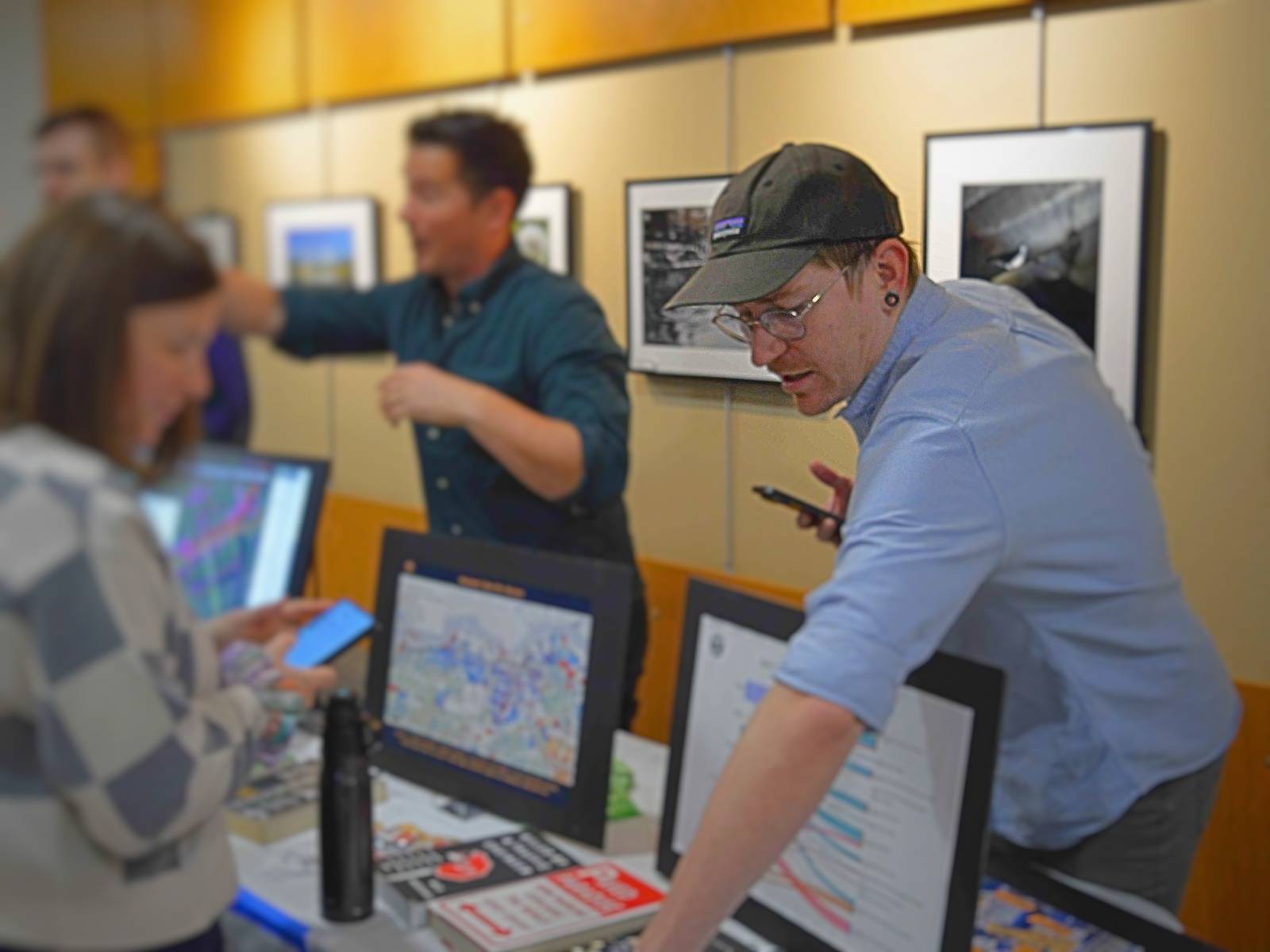 James Murchison in a cap and glasses at a Strong Towns Ottawa booth, leaning over the table to point at a chart while walking a resident through property tax-revenue data.